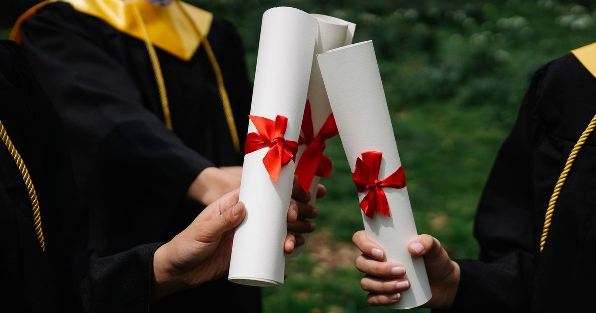 Mezuniyet cübbeli iki kişi kırmızı kurdeleli diploma rulolarını tutuyor