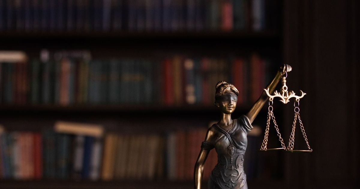 Kitap rafları önünde bronz adalet terazisi heykeli