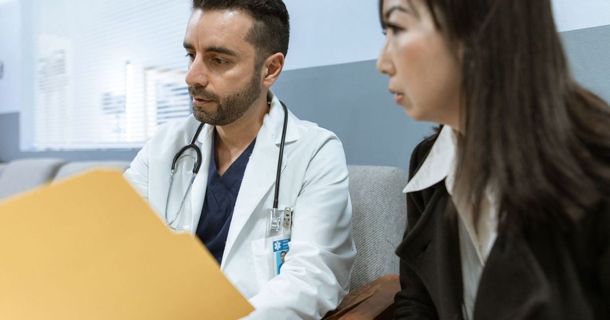 Beyaz önlüklü bir doktorun hastasıyla birlikte sarı bir dosyayı incelemesi